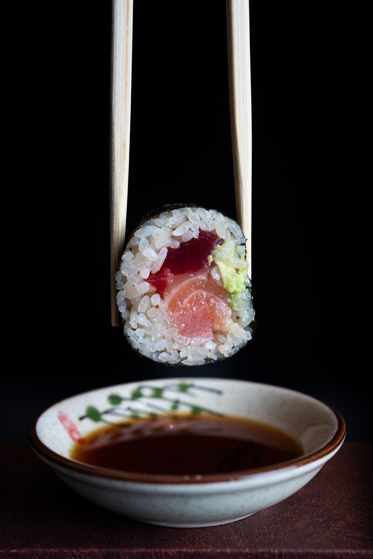 Futomaki sujeto con palillos sobre cuenco de salsa de soja
